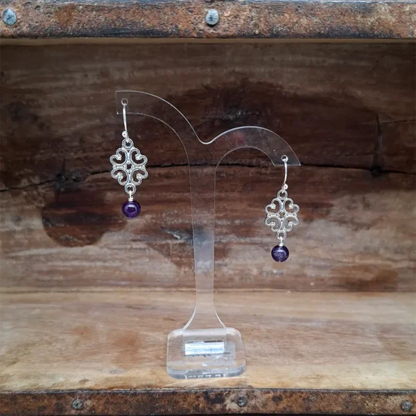 Amethyst Ohrringe mit echt silbernen Ohrhaken, an denen kleine versilberte Ornamente und Amethyst Perlen hängen.