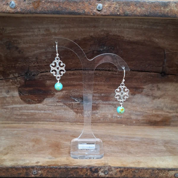 Silberne Ohrhaken mit verrschnörkelten Ornamenten an den unten eine türkise Perle hängt. Schöne, kleine, längliche Hängeohrringe